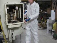 A man in white coveralls and goggles working on an object.